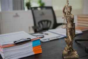 A desk with a statue holding a scale on it. desk chair and white wall background.